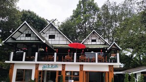 Un bâtiment à deux étages de style architectural traditionnel, doté d’un balcon agrémenté de meubles en bois et d’un parasol rouge.