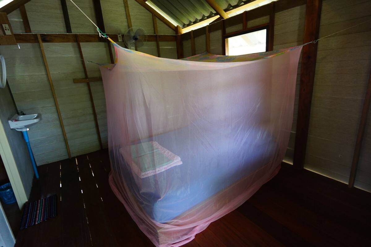 Una habitación con una cama cubierta por una mosquitera, vigas de madera en el techo, una ventana y un lavabo.