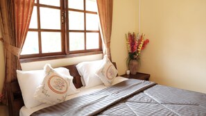 A neatly made bed with two decorative pillows, a wooden headboard, and a window with curtains.