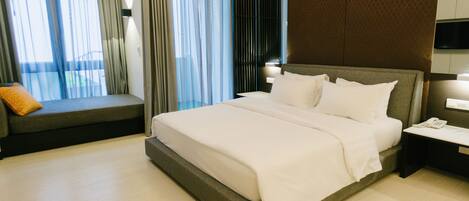 A modern hotel room with a large bed, a seating area with a cushion, and a bedside table with a phone.