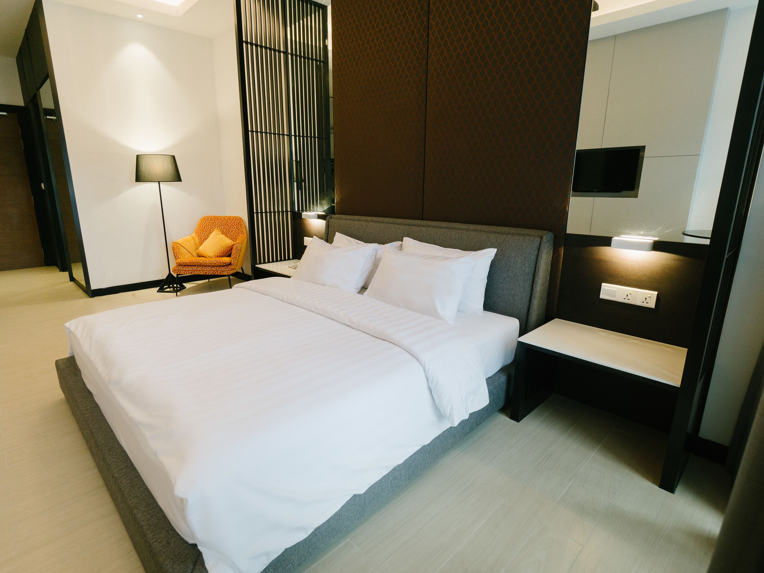 A neatly made bed with white linens, a grey upholstered headboard, and a bedside table with a lamp.
