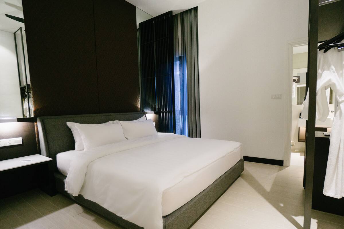 A modern hotel room with a large bed, a bedside table, a mirror, and a view of the bathroom.