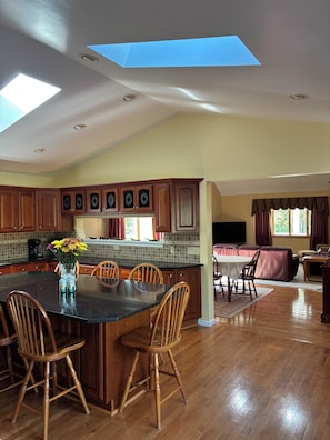 A spacious kitchen with wooden cabinets, a central island with chairs, and a skylight.