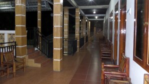 Un pasillo con pilares de madera, suelo de baldosas y sillas de madera dispuestas a lo largo de las paredes.
