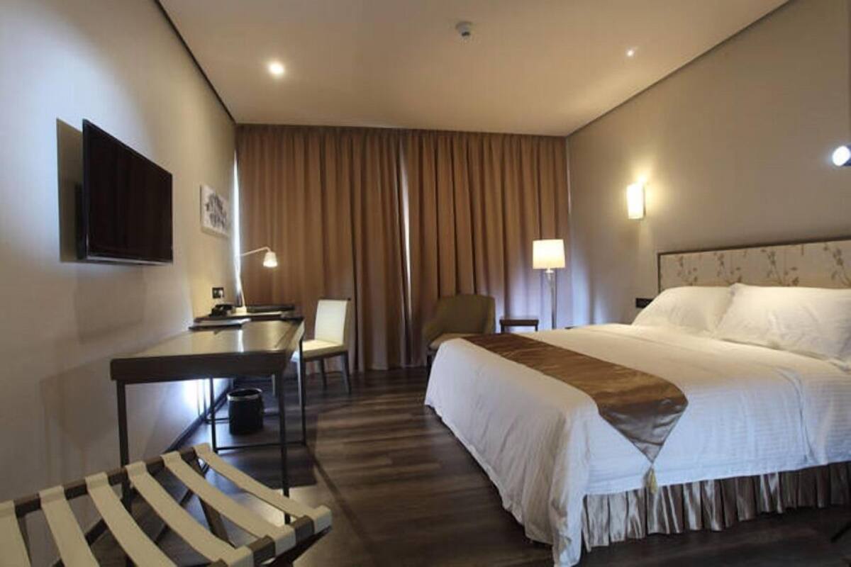 Una camera d'albergo con un letto, una scrivania, una sedia, una TV e una lampada.
