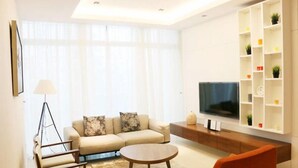 A modern living room with a sofa, armchair, coffee table, TV, and built-in shelving.
