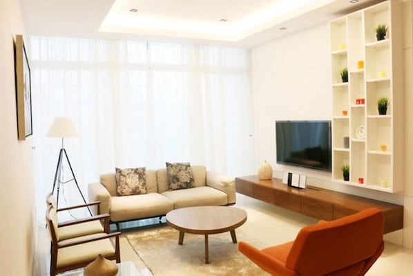 A modern living room with a sofa, armchair, coffee table, TV, and built-in shelving.