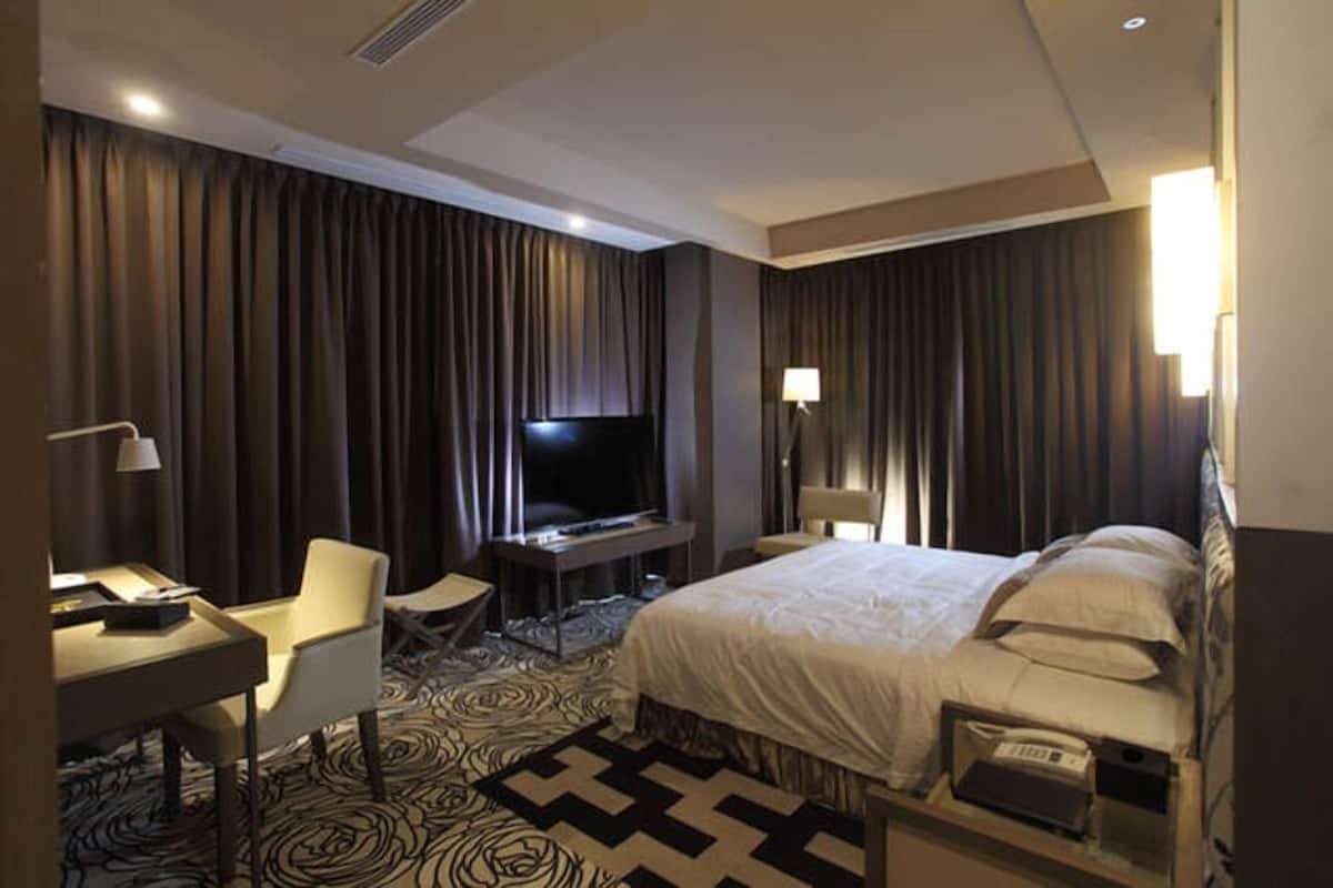Camera d'albergo con un letto grande, una scrivania con una sedia, un televisore e una lampada.