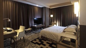 A hotel room with a large bed, a desk with a chair, a TV, and a lamp.