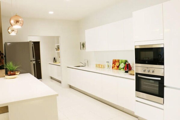 A modern kitchen with white cabinetry, a stainless steel oven, and a countertop with fruits and a kettle.