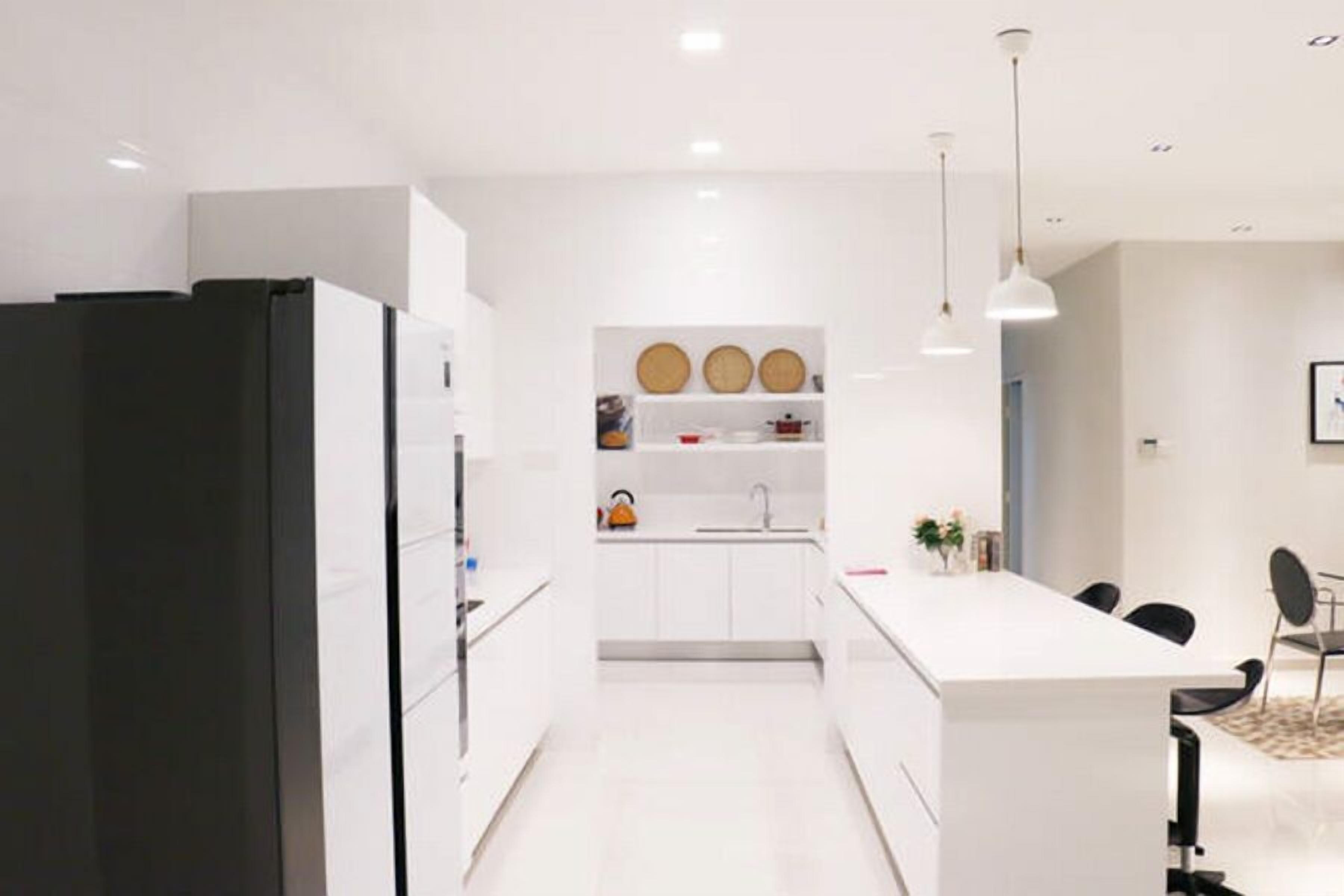 A modern kitchen with white cabinetry, a black refrigerator, a central island with seating, and pendant lighting.