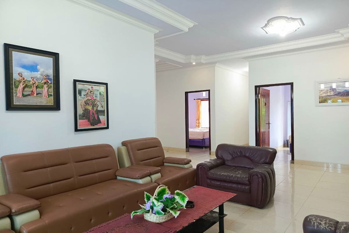 A living room with two brown sofas, a small table with a decorative plant, and two framed pictures on the wall.