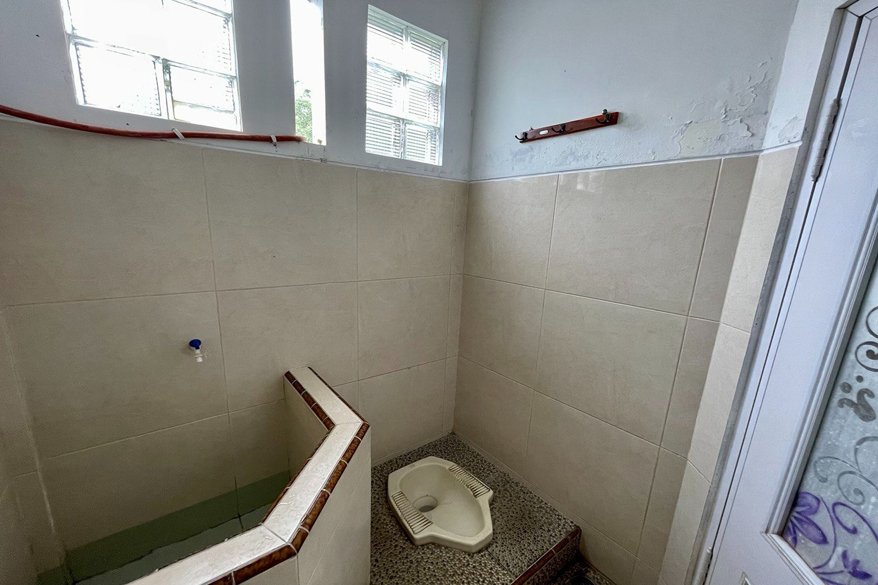 A small, tiled bathroom with a toilet, a shower, and a window.