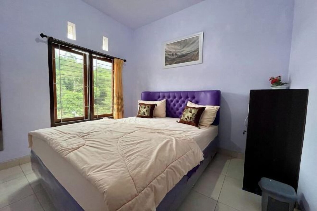 A bedroom with a bed, a headboard, a window, and a painting on the wall.