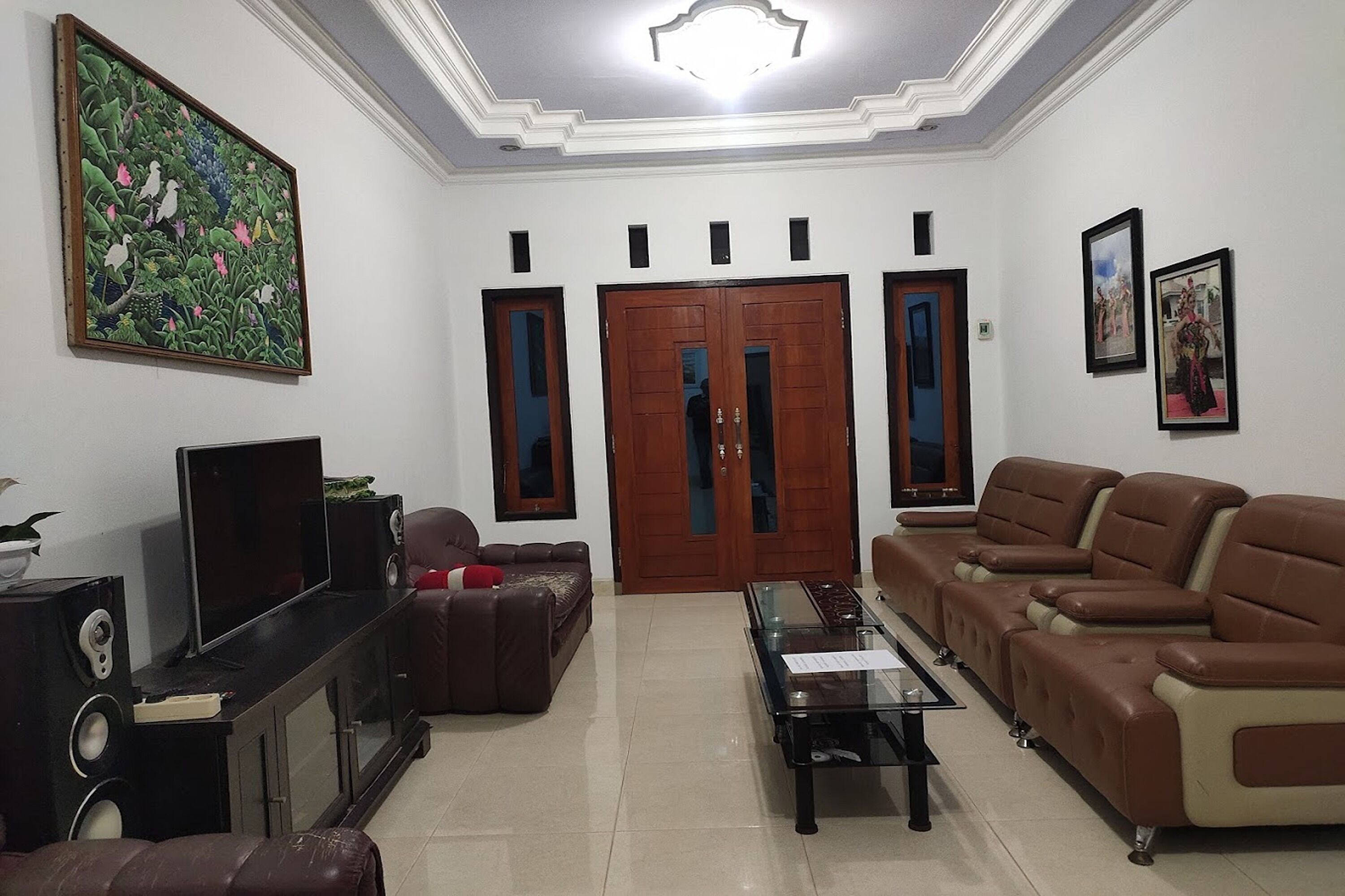 Una sala de estar con un televisor de pantalla plana grande, sofás de cuero, una mesa de centro de vidrio y un cuadro en la pared.