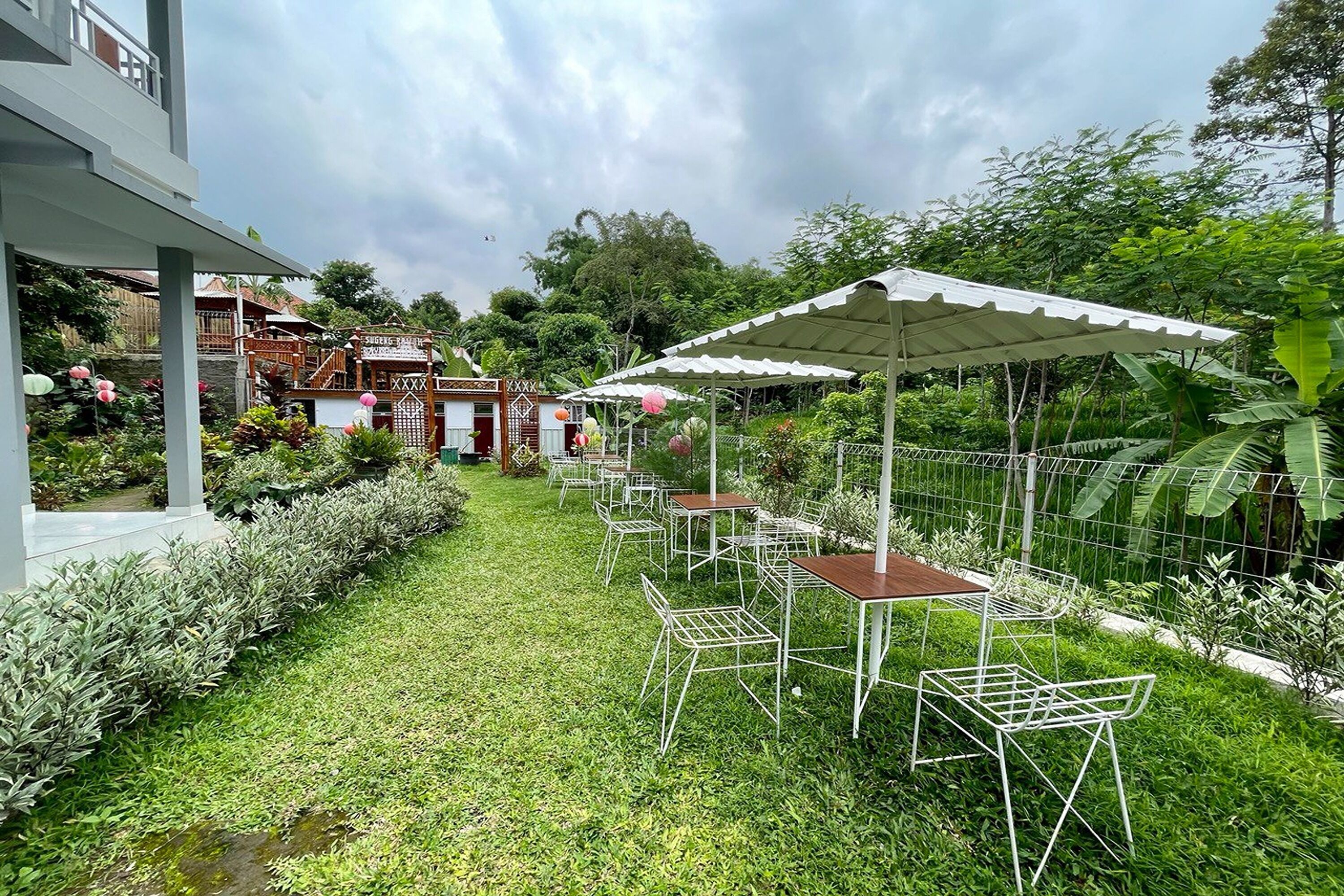 A well-maintained garden with a patio area featuring tables and chairs, surrounded by lush greenery and a fence.