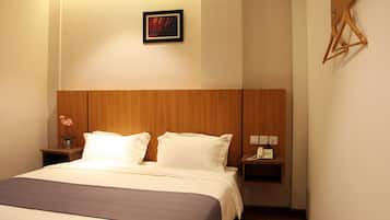 Habitación de hotel con cabecera de madera, cama con ropa blanca, mesita de noche con un teléfono y un jarrón de flores, y una obra de arte colgada en la pared.