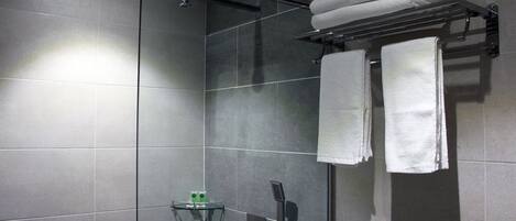 Un área de ducha moderna con cabina de vidrio, un perchero con toallas dobladas y un estante pequeño con artículos de aseo.