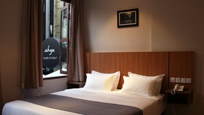 Una habitación de hotel con cama, mesita de noche con teléfono, ventana con cortinas e imagen en un marco en la pared.