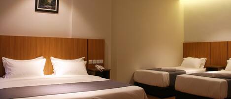 Quarto de hotel com uma cama grande, duas camas menores, uma mesinha de cabeceira com telefone e um quadro na parede.