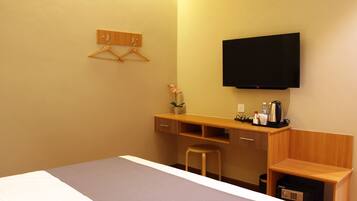 Habitación de hotel con cama, escritorio con silla, televisor montado en la pared y un taburete pequeño.