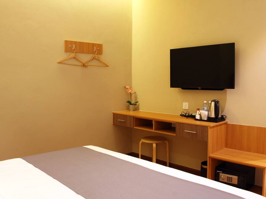 Habitación de hotel con cama, escritorio con silla, televisor montado en la pared y un taburete pequeño.