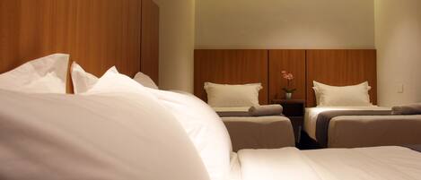 A hotel room with a large bed, two smaller beds, a nightstand with a vase of flowers, and wooden paneling on the walls.
