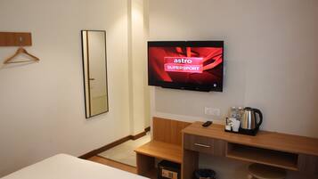 Habitación de hotel con cama, un escritorio de madera, un televisor mostrando 'astro SUPERSPORT', un espejo y un cesto de basura.
