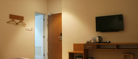 Habitación de hotel con cama, televisor montado en la pared, escritorio de madera con tetera y un taburete pequeño.