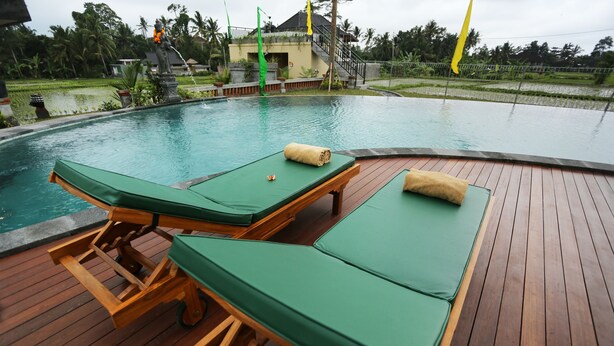 A poolside area with wooden loungers and a statue. - Darra Ria Villa Ubud (Ubud)