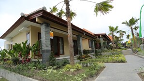 A residential building with a tiled roof, stone pillars, and a well-maintained garden with various plants and a concrete pathway. - Darra Ria Villa Ubud (Ubud)