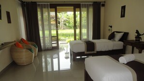 A hotel room with two beds, a large window with curtains, a wicker chair, and a small table with a lamp. - Darra Ria Villa Ubud (Ubud)