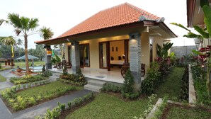 A two-story house with a tiled roof, a porch with a table and chairs, and a well-maintained garden with various plants and a small pool. - Darra Ria Villa Ubud (Ubud)