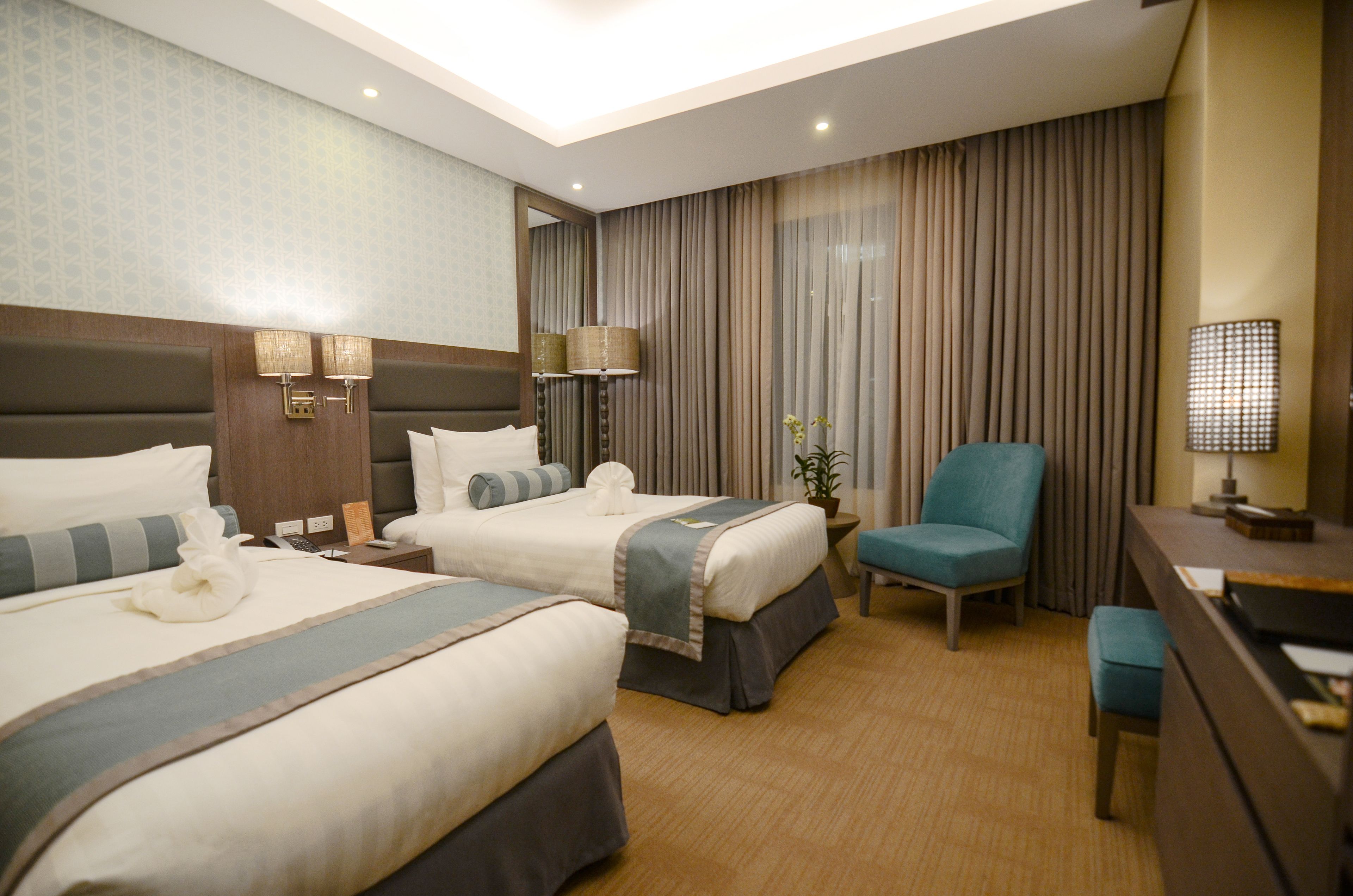 A hotel room with two beds, a desk, a chair, and a large window with curtains.