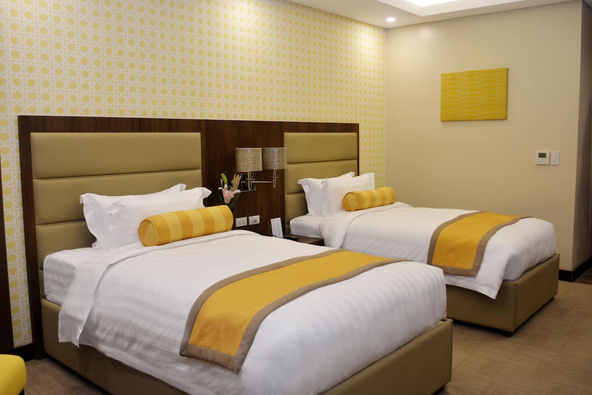 Ein Hotelzimmer mit zwei Betten, jeweils mit Kopfteil, weißer Bettwäsche und einem gelben Akzent.