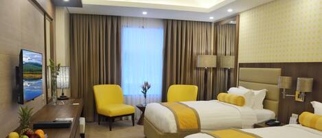 Une chambre d’hôtel avec deux lits, un bureau avec une télévision, une chaise et un panier de fruits.