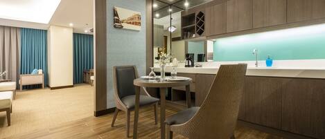 A modern hotel room with a dining area, a kitchen, and a large window.