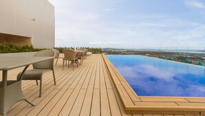 Un espace piscine aménagé sur le toit, avec une terrasse en bois, des sièges d’extérieur et une vue sur le paysage urbain.