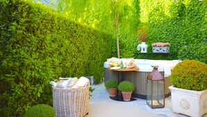 A garden area with a hot tub, wicker furniture, potted plants, and a lantern.