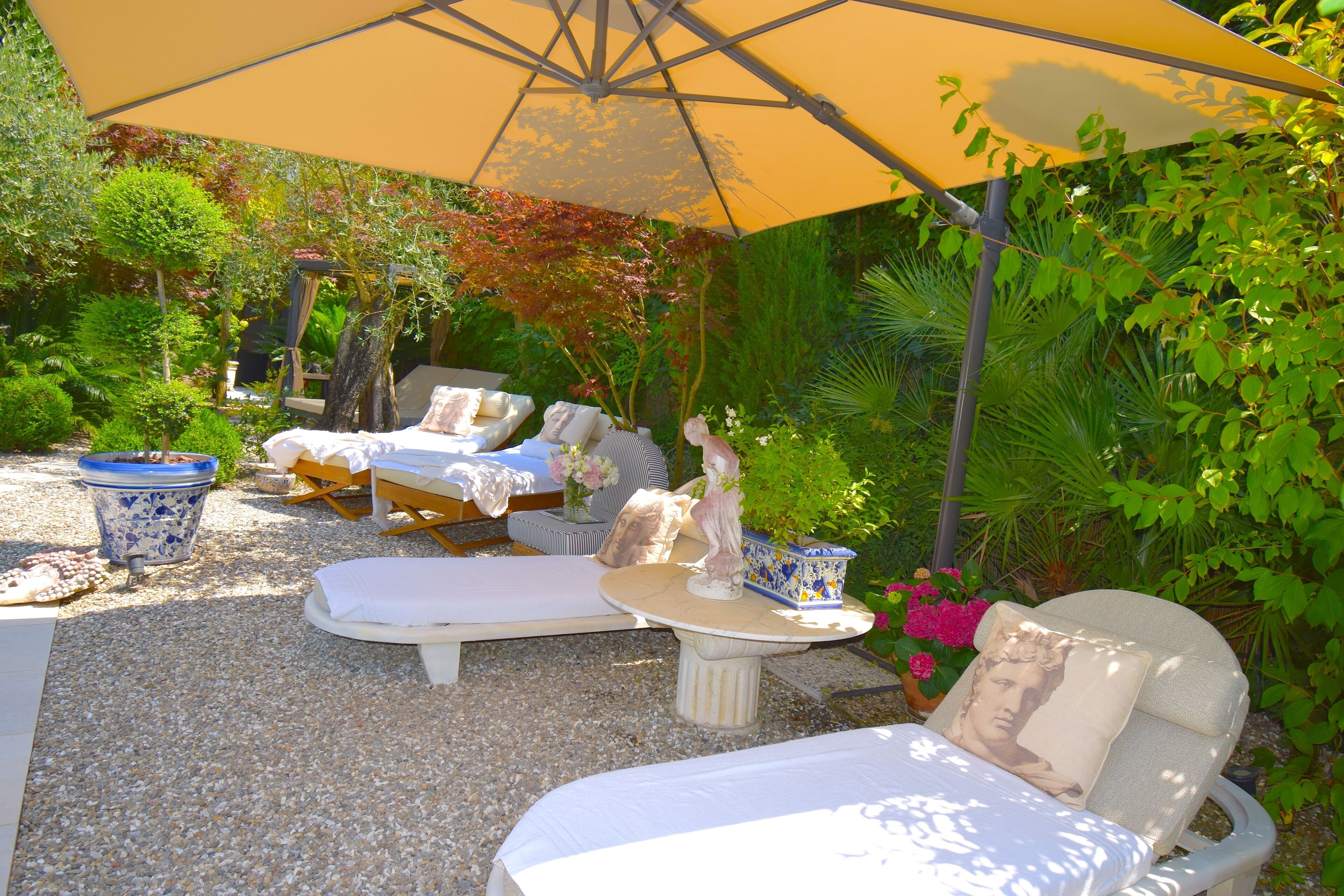 An outdoor seating area with a table and chairs, surrounded by plants and a large umbrella.