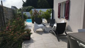 Een terras met een zwembad, tuinmeubels en potplanten.