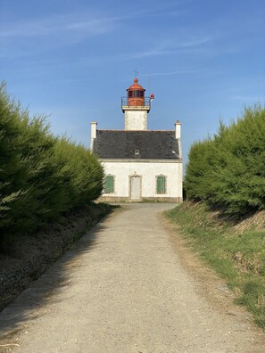 Un phare, accessible par un sentier de gravier, et entouré de verdure.