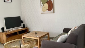 Una sala de estar moderna con un sofá gris, una mesa de centro de madera, una silla de mimbre y un televisor de pantalla plana sobre un mueble de madera.