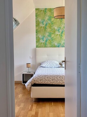 Een slaapkamer met een bed, nachtkastje, lamp en een muur met een bladmotief.