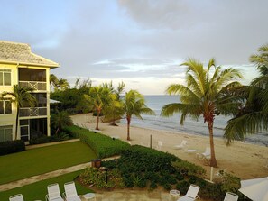 A beachfront property with a two-story building, a well-maintained lawn, and a sandy beach with lounge chairs.