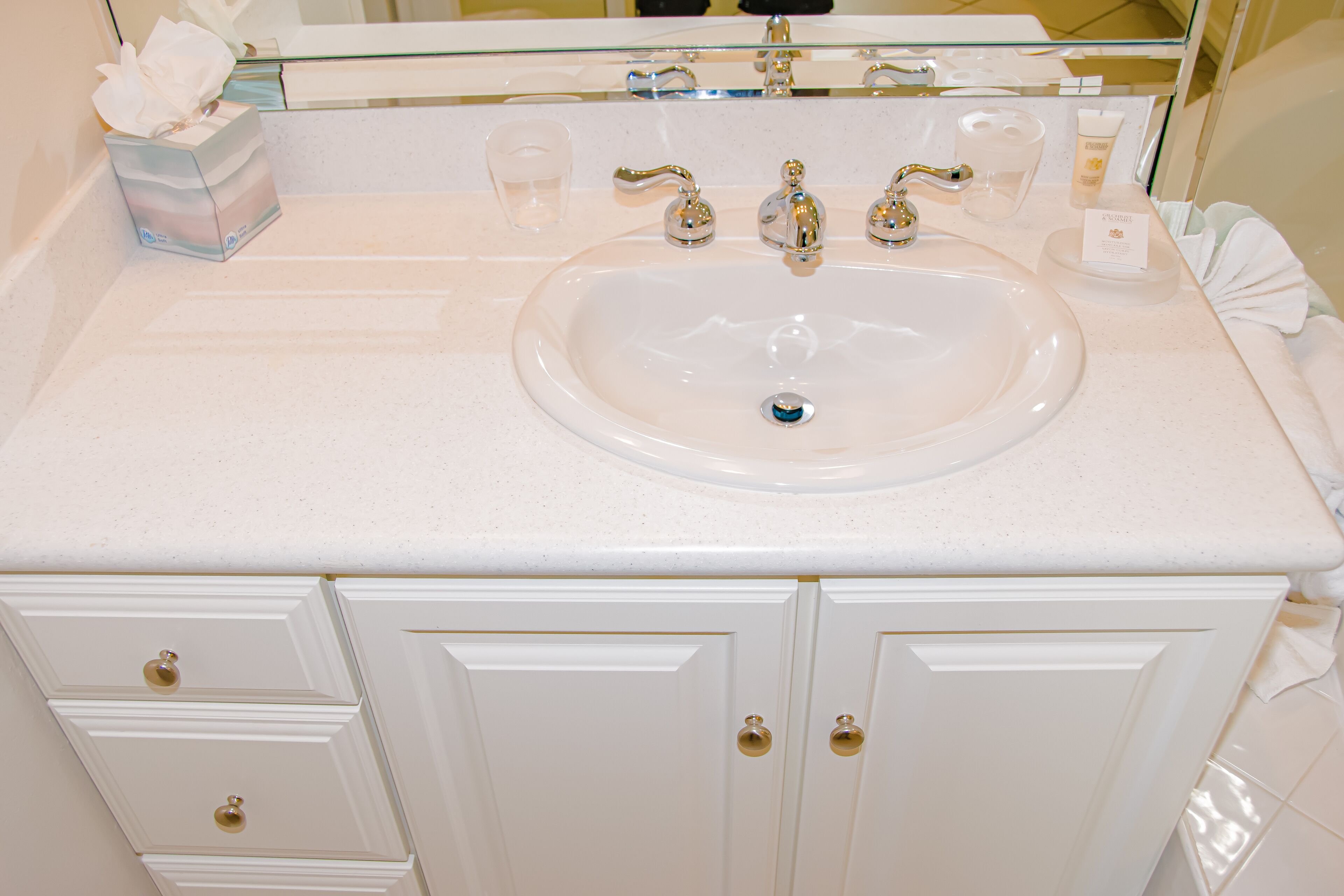 Une salle de bain avec un lavabo blanc, deux robinets, un miroir et un boîte à mouchoirs.