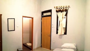A bedroom with a bed, a door, a small trash bin, and a window with curtains. - Adikarta Guesthouse Janti (Banguntapan)