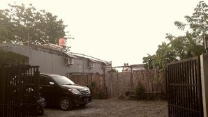 A gated area with a parked car, a building with a tiled roof, and a wooden fence. - Adikarta Guesthouse Janti (Banguntapan)