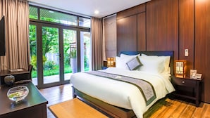 A modern bedroom with a large bed, bedside lamps, a nightstand, and a view of greenery outside. - Dai An Phu Villa (Da Nang)