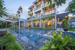 Un hotel moderno con piscina, mobiliario exterior y abundante vegetación.